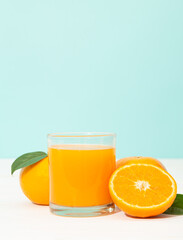 Fresh orange juice in glass and oranges fruit on white wooden table with blue background with copy space.