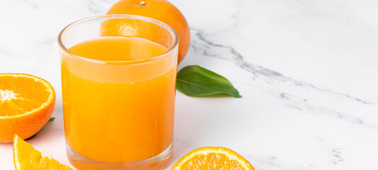 Fresh orange juice in glass and oranges fruit on white marble table banner background with copy space.