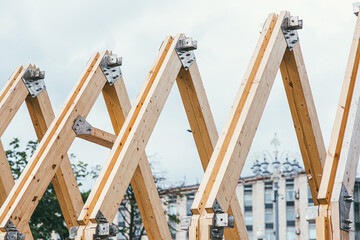 Wooden rafters of unfinished roof against the background of the city and white sky. The concept of building and creating new housing