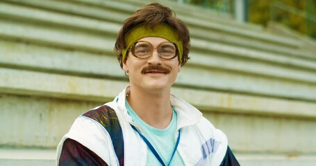 Close up portrait of cheerful handsome Caucasian man in big glasses turning his head and smiling to camera outdoors. Joyful funny retro style male with mustache in good mood. 60s concept