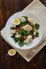 Vegetarian food fresh vegetable salad cauliflower cherry tomato cucumber sesame seed black olives with parsley and lettuce. The concept of healthy food and dieting. No people