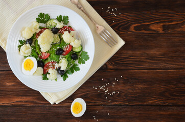 Super food fresh vegetable salad cauliflower cherry tomato cucumber sesame seed black olives with parsley and lettuce close up top view. The concept of healthy food and dieting. Copy space text