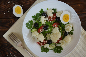Vegetarian food fresh vegetable salad cauliflower cherry tomato cucumber sesame seed black olives with parsley and lettuce. The concept of healthy food and dieting. No people