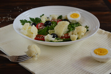 Vegetarian food fresh vegetable salad cauliflower cherry tomato cucumber sesame seed black olives with parsley and lettuce. The concept of healthy food and dieting. No people