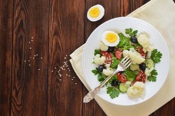 Super food fresh vegetable salad cauliflower cherry tomato cucumber sesame seed black olives with parsley and lettuce close up top view. The concept of healthy food and dieting. Copy space text