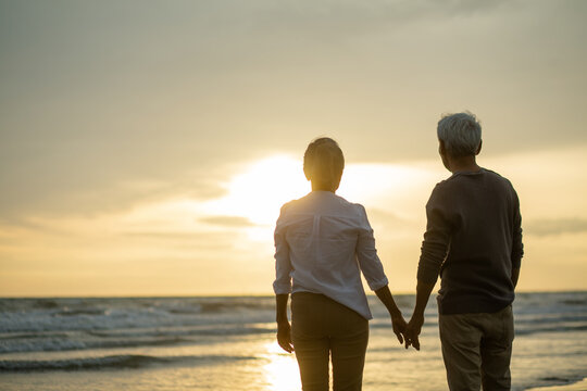 Romantic senior couple standing holding hands at each other .on beach during sunset near sea,  .Retirement age concept and love, copy space for text
