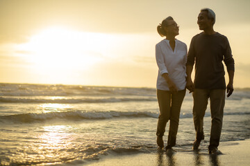 Romantic couple senior stroll travel on beach near the sea at sunset..Retirement age concept and love, copy space for text