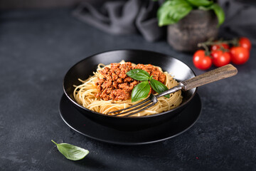 Spaghetti bolognese in a black plate on a dark background , italian cuisine. 