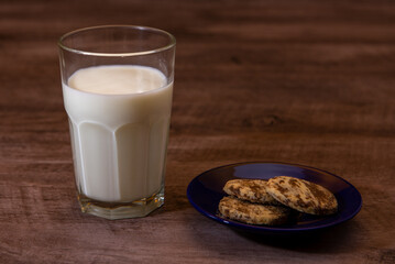 Leche en vaso de vidrio transparente con galletas de chocolate y vainilla sobre madera 