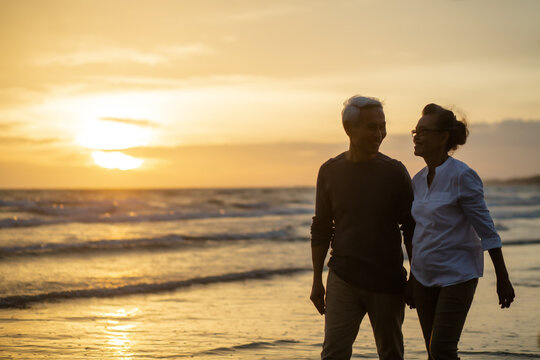 Happy Romantic of senior man laughing while Walking the beach together,.on sandy beach during sunset,  .Retirement age concept and love, copy space for text