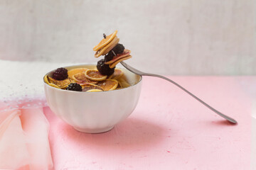 Mini pancakes with blackberry white dishes on a pink table. A new trend dessert in social networks. Little Dutch poffertjes.