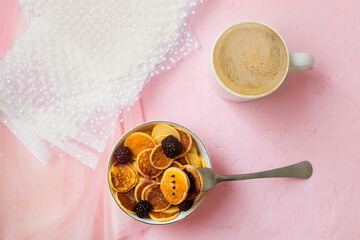 Mini pancakes with blackberry white dishes on a pink table. A new trend dessert in social networks. Little Dutch poffertjes.
