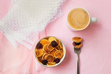 Mini pancakes with blackberry white dishes on a pink table. A new trend dessert in social networks. Little Dutch poffertjes.