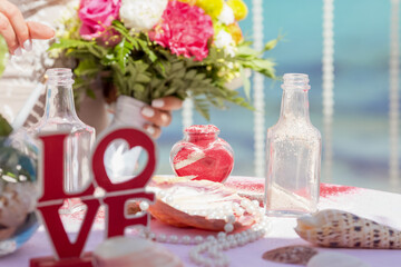 Bride and groom pouring colorful different colored sands into the crystal vase close up during symbolic nautical decor destination wedding marriage unity ceremony on sandy beach in front of the ocean 