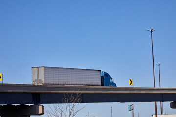 Big silver and blue truck in motion going over a freeway bridge against a blue sky