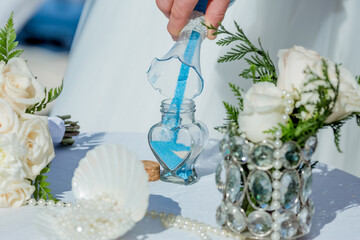 Bride and groom pouring colorful different colored sands into the crystal vase close up during symbolic nautical decor destination wedding marriage unity ceremony on sandy beach in front of the ocean 