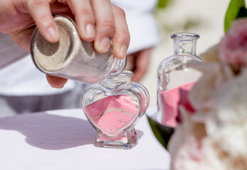 Bride and groom pouring colorful different colored sands into the crystal vase close up during symbolic nautical decor destination wedding marriage unity ceremony on sandy beach in front of the ocean 