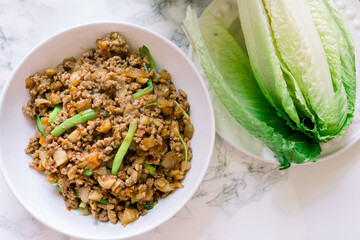 A Head of Green Lettuce and a White Bowl with Ground Chicken with Water Chestnuts for Lettuce Wraps. 