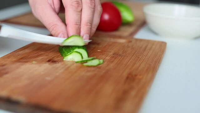 Close up view of a process of preparing healthy food. Slicing cucumbers for salad.