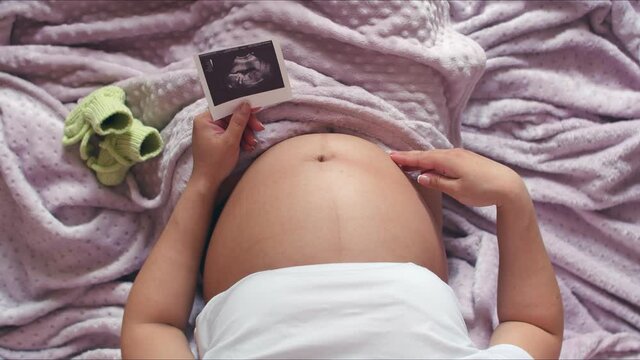 A pregnant girl, stroking his hand and holding a photo with an ultrasound.