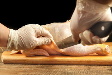 Fototapeta na wymiar A female hand in gloves cuts off chicken pieces with a sharp knife.
