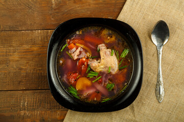 Black dish of vegetable soup on a tablecloth on a wooden table.