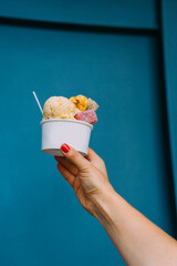 Woman hand holding an ice cream cup with colorful gums on a blue background