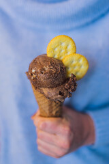 Woman hand holding a cone  with chocolate ice cream and crakers on a blue background