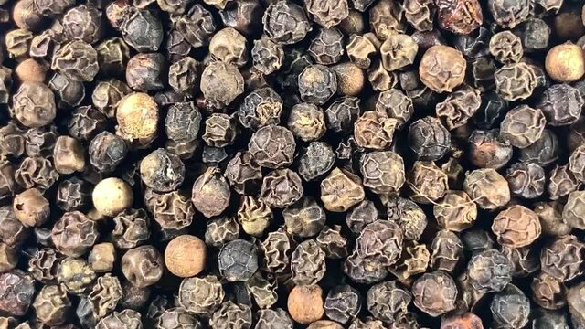 Grains of black pepper peas close-up rotate clockwise. Top view