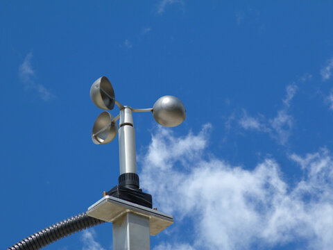 anemometer wind speed indicator measuring device fixed to aluminum bracket on tube post. meteorological device. abstract low angle view. spoon shaped semi sphere blades. clear blue sky. white clouds