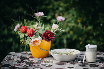 Stimmungsvolles Stilleben mit Blumen, Salatschüssel mit Gurkensalat und Dressing im Glas mit einer Kelle. Selektive Schärfe