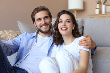 Portrait young family of happy husband and wife sitting in sofa cuddle looking at camera posing, smiling young couple relax at home together