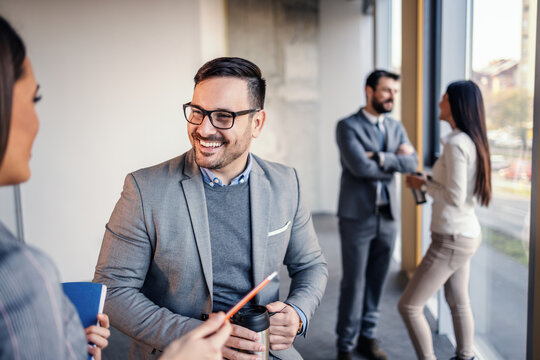 Handsome Smiling Friendly Caucasian Architect Holding Thermos With Coffee And Talking With His Colleague. In Background Are Other Two Colleagues. They All Taking A Break From Hard Work.