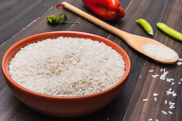 Rice in a bowl, vegetables and wooden spoon on a brown wooden surface