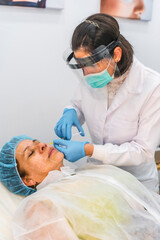A doctor with a screen and face mask applying injections with safety measures to a patient with a...
