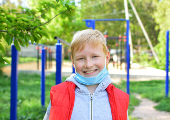 A smiling boy in the street took off a medical protective mask of the playground. Face mask for protection coronavirus outbreak. Quarantine end concept. Allergy concept in children, air pollution.