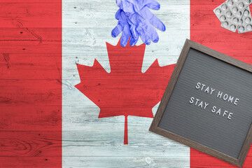 Canada flag background on wooden table. Stay Home writing board, surgery gloves, pills with minimal national Covid 19 concept.