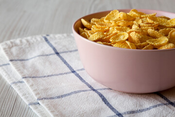 Corn flakes in a pink bowl for breakfast over white wooden surface, side view. Space for text.