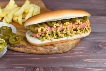 Homemade hot dog with pickles, fries and mustard on wood background.