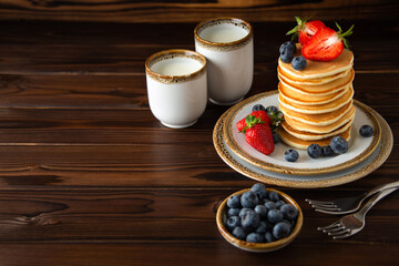 Cassic american pancakes with fresh blueberries, strawberries and two caps of milk.