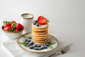 Stack of pancakes with fresh blueberries, strawberries, powdered sugar and cap of milk. Sweet summer breakfast.