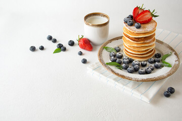 Homemade american pancakes with fresh blueberries, strawberries powdered sugar and glass of milk. Summer breakfast.