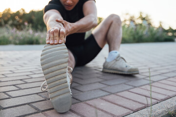 Man does stretching exercises on paving tile in outdoor park