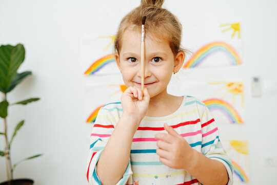 Portrait of happy preschool girl with brush in front of rainbow paintings