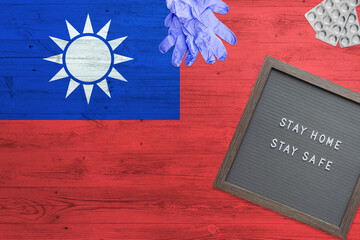 Taiwan flag background on wooden table. Stay Home writing board, surgery gloves, pills with minimal national Covid 19 concept.