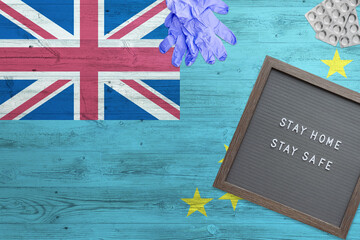 Tuvalu flag background on wooden table. Stay Home writing board, surgery gloves, pills with minimal...