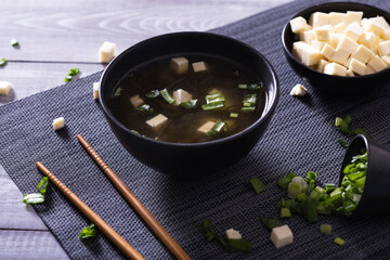 Japanese hot miso soup in a black bowl on the wooden table. Horizontal view from above