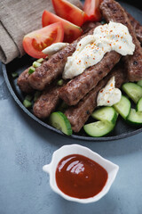 Closeup of roasted serbian cevapi or cevapcici sausages with kajmak cheese and vegetables, selective focus, vertical shot
