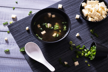 Japanese hot miso soup in a black bowl on the wooden table. Horizontal view from above