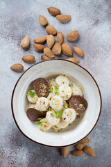 Bowl of vareniki or curd dumplings with chocolate chips and nuts, top view on a beige stone surface, vertical shot